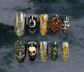 Ten press-on nails with a gothic pirate-themed design are arranged in two rows against a dark, textured background. Designs include silver with gothic lettering, a pirate flag skull and pirate ship that change with temperature, silver and gold filigree design, a spinning ship wheel, and iridescent green/purple reminiscent of black pearls. 