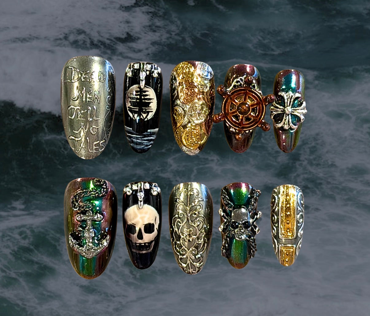 Ten press-on nails with a gothic pirate-themed design are arranged in two rows against a dark, textured background. Designs include silver with gothic lettering, a pirate flag skull and pirate ship that change with temperature, silver and gold filigree design, a spinning ship wheel, and iridescent green/purple reminiscent of black pearls. 