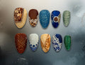 Ten decorative press-on nails arranged in two rows on a dark textured background, featuring embossed scrollwork, painted ceramic and porcelain tile, and sculpted pressed glass patterns 
