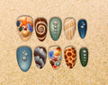 Ten hand-painted press-on nails with sculpted seashells, starfish, pearls and sea-glass details in coastal blues, greens and sandy neutrals.