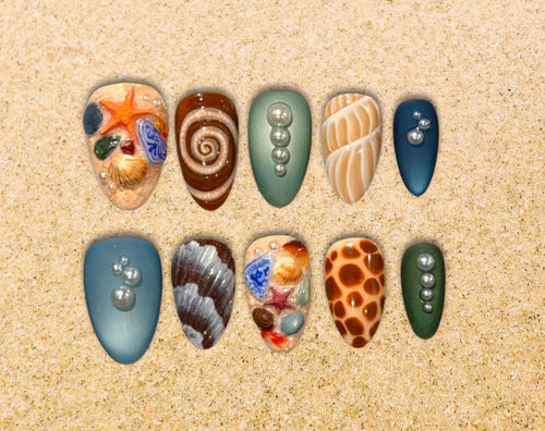 Ten hand-painted press-on nails with sculpted seashells, starfish, pearls and sea-glass details in coastal blues, greens and sandy neutrals.
