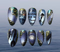 Ten press-on nails arranged in two rows against a soft blue water background. The nails feature various fantasy and gothic designs, including a mermaid silhouette, a pirate ship, handwritten text reading 'Follow her sound and be forever bound', a mermaid tail, and ornate gold filigree patterns on a purple, blue, and black glittery base.
