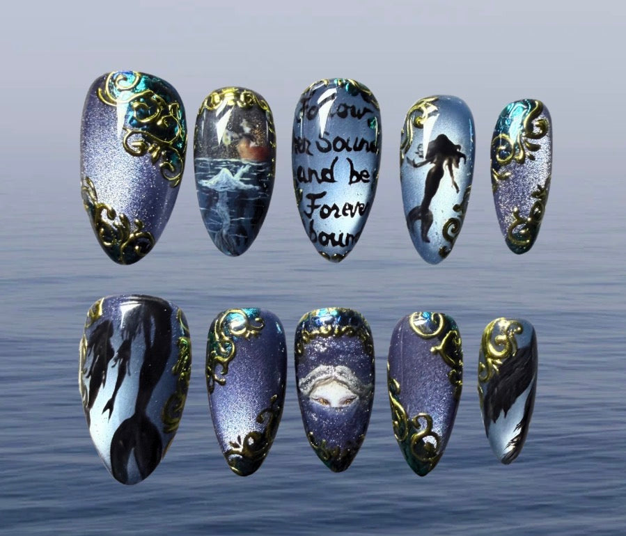Ten press-on nails arranged in two rows against a soft blue water background. The nails feature various fantasy and gothic designs, including a mermaid silhouette, a pirate ship, handwritten text reading 'Follow her sound and be forever bound', a mermaid tail, and ornate gold filigree patterns on a purple, blue, and black glittery base.