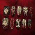 Luxury gothic press-on nail set in translucent oxblood red and black, featuring antique silver filigree, black lace, ruby-red crystals, ornate jeweled embellishments, and a silver skull motif.