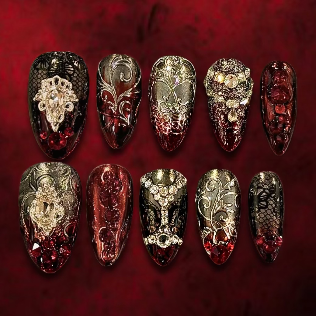 Luxury gothic press-on nail set in translucent oxblood red and black, featuring antique silver filigree, black lace, ruby-red crystals, ornate jeweled embellishments, and a silver skull motif.