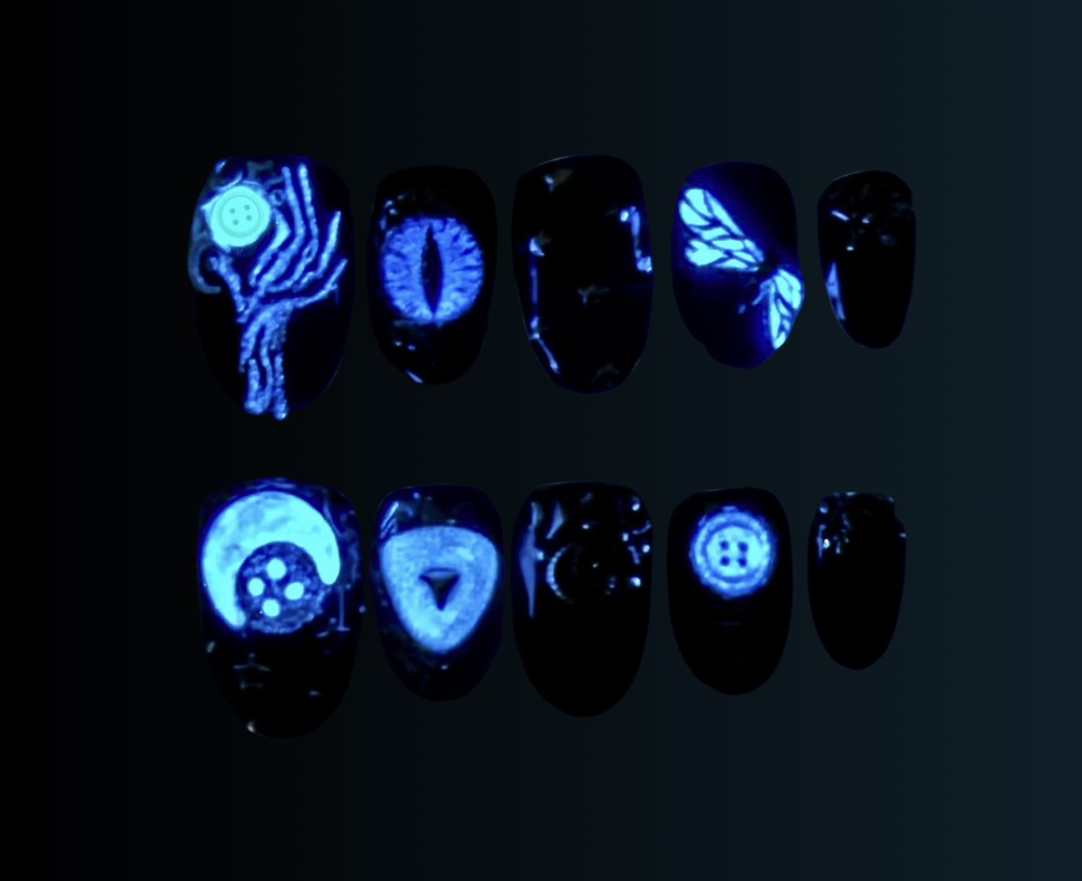 Coraline-inspired press-on nail set in midnight blue with antique silver filigree, celestial stars, button and key details, cat-eye accents, and hidden glow-in-the-dark elements.