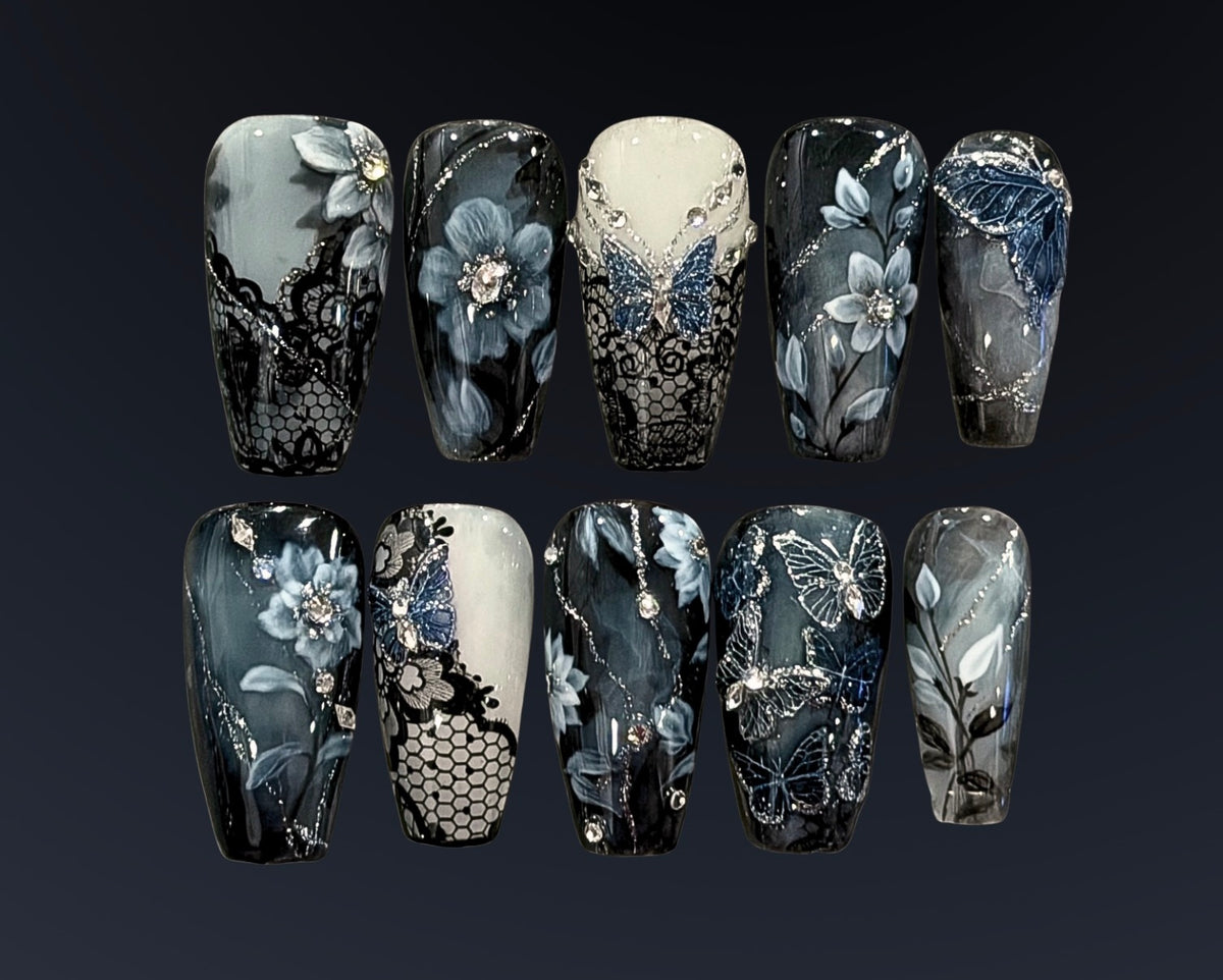 Gothic bridal press-on nails in misty blue, black, and ivory with hand-painted flowers, black lace, silver butterflies, crystals, and delicate silver detailing.