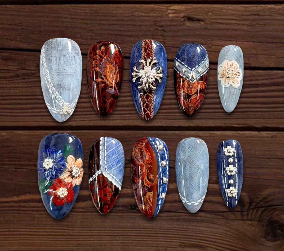 Luxury Western-inspired press-on nails with blue denim texture, paisley patchwork, contrast stitching, silver studs, conchos, and floral accents.