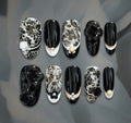 Luxury black and ivory floral press-on nails with sculptural camellia flowers, pearl accents, and delicate gold detailing.