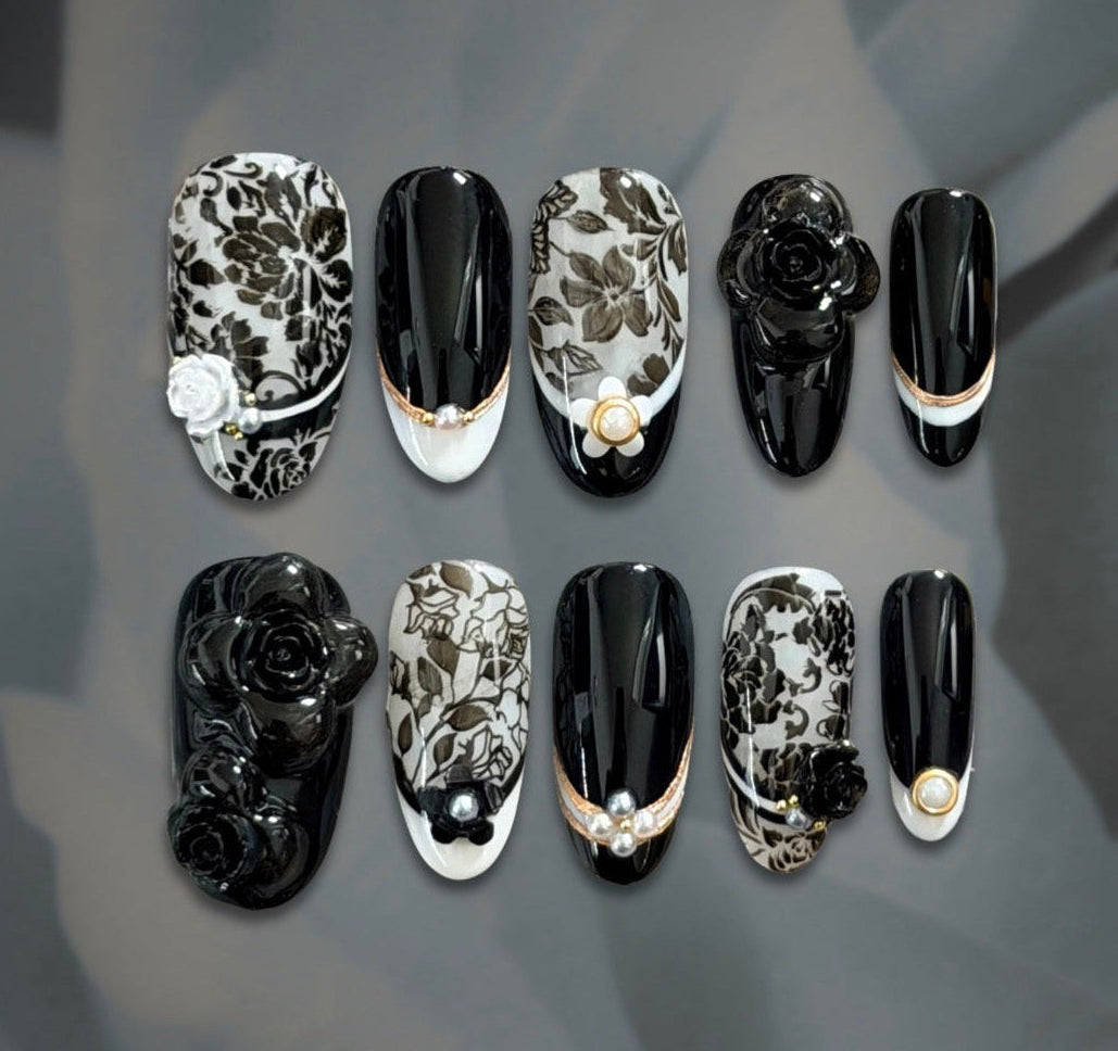 Luxury black and ivory floral press-on nails with sculptural camellia flowers, pearl accents, and delicate gold detailing.
