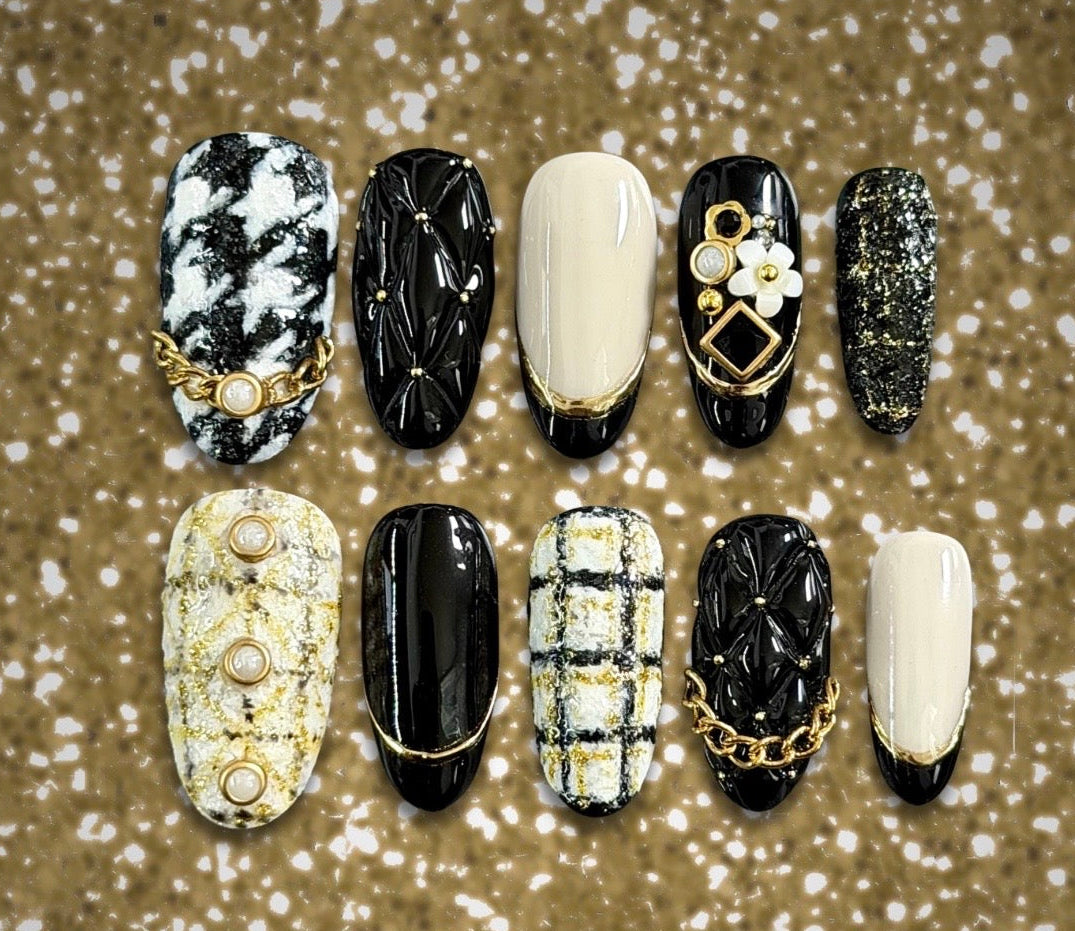 Luxury black and ivory tweed press-on nails with quilted texture, gold chains, pearl accents, and floral jewelry details.